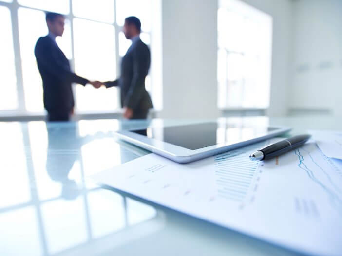 two blurry business people shaking hands behind a conference table